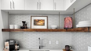 A kitchen with a white countertop, a stainless steel sink, a coffee maker, and a framed picture on the wall. - DeLuna Vista the Brent Lofts (Pensacola)