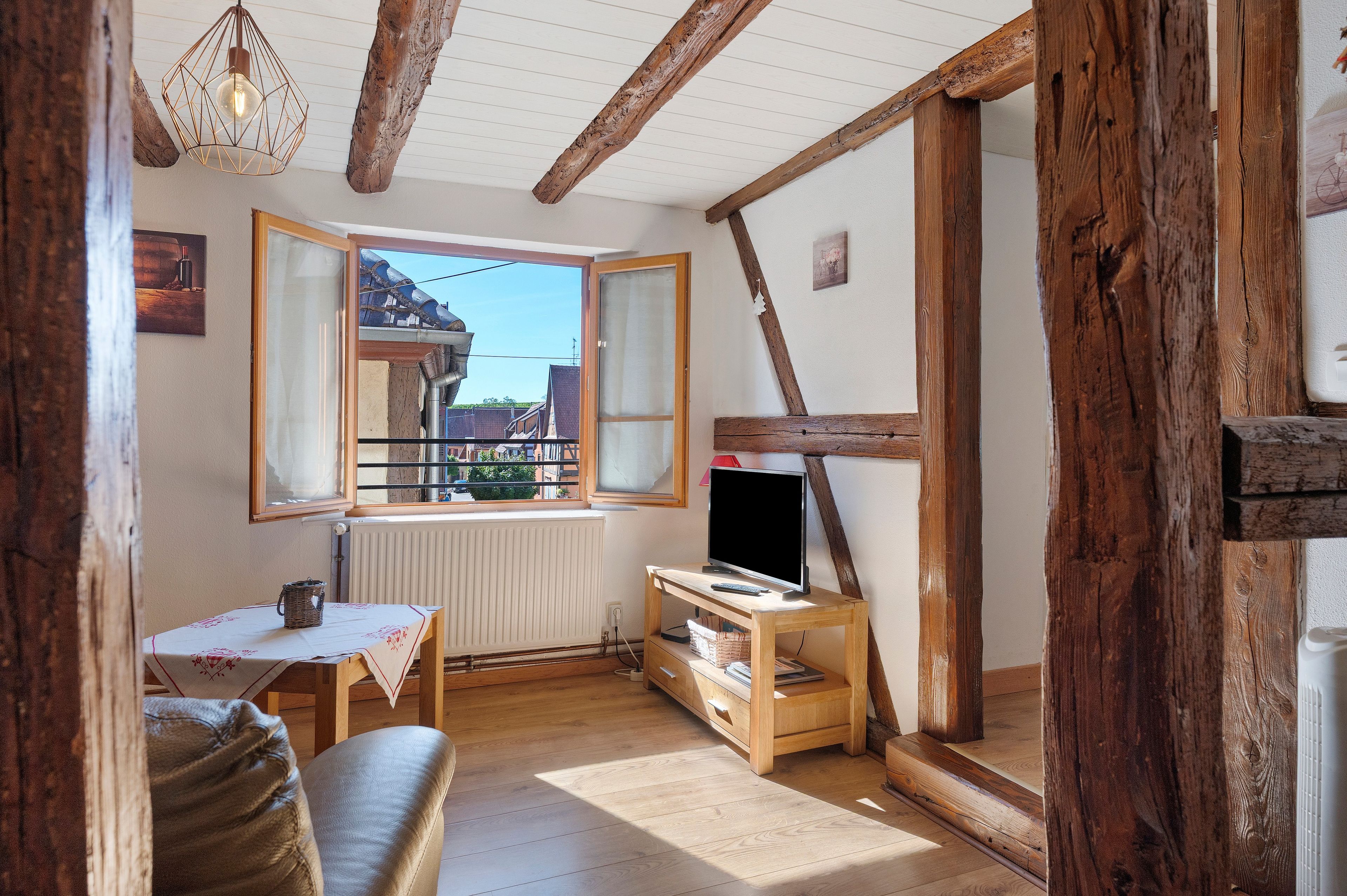 Una habitación acogedora con techo de madera, una mesa con mantel blanco, un sofá y un televisor sobre un mueble de madera.