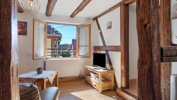 Una habitación acogedora con techo de madera, una mesa con mantel blanco, un sofá y un televisor sobre un mueble de madera.