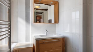 A bathroom with a white sink, wooden vanity, and a mirror with a wooden frame. - Gîtes les cigogneaux - Gîte Pinot (Beblenheim)