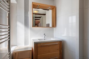Un baño con un lavamanos blanco, tocador de madera y un espejo con marco de madera.