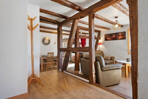 Interior rústic amb bigues de fusta a la vista, un sofà de cuir, zona de menjador i un rellotge penjat a la paret.