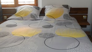 A bed with a patterned bedspread and pillows, a wooden headboard, and a window with blinds.