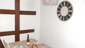 A dining area with a wooden table set for four, a wall clock, and a copper pendant light.