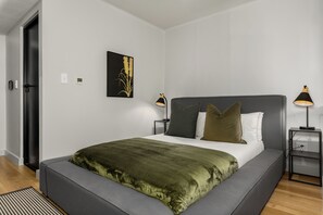 A modern bedroom with a large bed, bedside lamps, a wall-mounted thermostat, and a framed picture. - Skyline Tokyo Studio w/ Table Mountain Views & Rooftop Pool and Lounge (Cape Town)