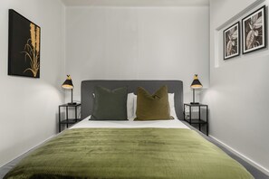 Een slaapkamer met een bed, twee nachtkastjes, twee lampen, een hoofdbord en kunstwerken aan de muur.
