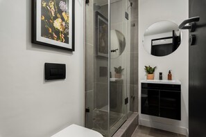 Een moderne badkamer met een douchecabine van glas, een wit wastafelmeubel met spiegel en een bloemrijk kunstwerk in een lijst aan de muur.