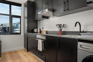 Een moderne keuken met donkere kastjes, een roestvrijstalen fornuis, een inbouwoven en een raam met uitzicht op een stadsbeeld.