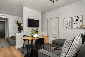 A modern living room with a grey sofa, a dining table with chairs, and a flat-screen TV mounted on the wall. - Skyline Tokyo Studio w/ Table Mountain Views & Rooftop Pool and Lounge (Cape Town)