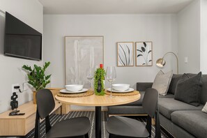 Een moderne woonkamer met een ronde eettafel, zwarte stoelen, een grijze bank en twee ingelijste kunstwerken aan de muur.