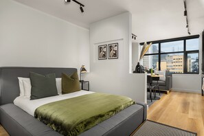 A modern bedroom with a large bed, a desk, and a view of the city through a large window. - Skyline Tokyo Studio w/ Table Mountain Views & Rooftop Pool and Lounge (Cape Town)
