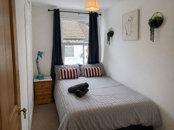 Une chambre à coucher comprenant un lit, une table de chevet, une lampe, une fenêtre avec des rideaux et des plantes fixées au mur.