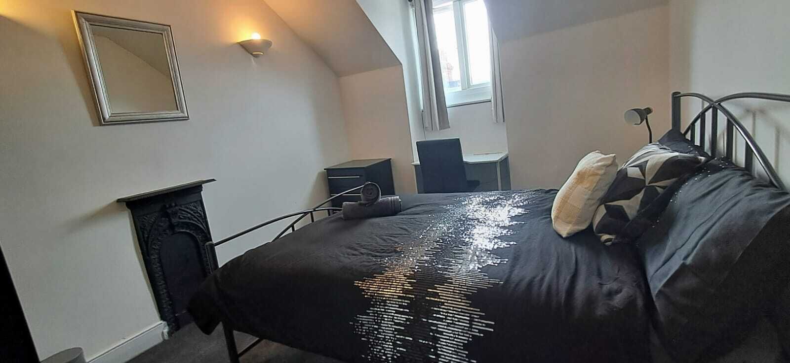 A bedroom with a bed, a desk, a chair, a mirror, and a window.