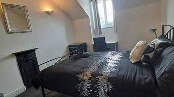 A bedroom with a bed, a desk, a chair, a mirror, and a window.