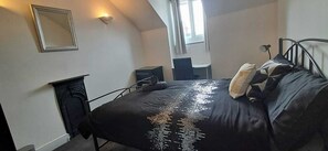 A bedroom with a bed, a desk, a chair, a mirror, and a window.