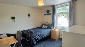 Ein Schlafzimmer mit Bett, Nachttisch, Schreibtisch, Stuhl und einem Fenster mit Vorhängen.