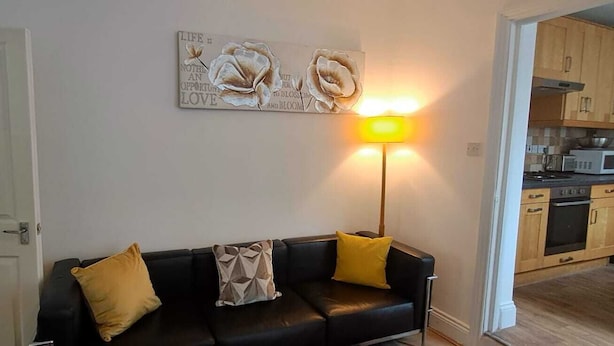 Ein Wohnzimmer mit einem schwarzen Ledersofa, zwei gelben Kissen, einem Wandbild und einer Stehlampe.