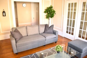 A grey sofa with cushions, a glass coffee table with a plant, and a wooden floor. - Great Apartment Conveniently Located (San Francisco)