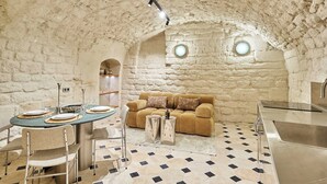 A cozy interior with a stone wall, a round table set for dining, a sofa, and a kitchen area. - Sublim new Triplex on Place des Vosges (Paris)
