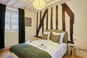 Ein Schlafzimmer mit einem Bett, einem Fenster mit Vorhängen, einer Wand mit freiliegenden Holzbalken und einer Hängelampe.
