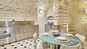 A modern kitchen with a stone wall, stainless steel appliances, and a dining area with a round table set for four. - Sublim new Triplex on Place des Vosges (Paris)