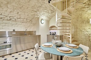Eine moderne Küche mit Steinwand, Edelstahlgeräten und einem Essbereich mit rundem Tisch für vier Personen.