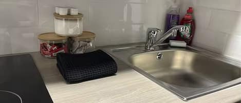 A kitchen with a stainless steel sink, a black electric stove, and storage jars on the counter.