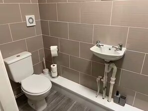 A bathroom with a toilet, a sink, and a toilet paper holder. - Modern Studio Mins from City Centre + Parking (Salford)