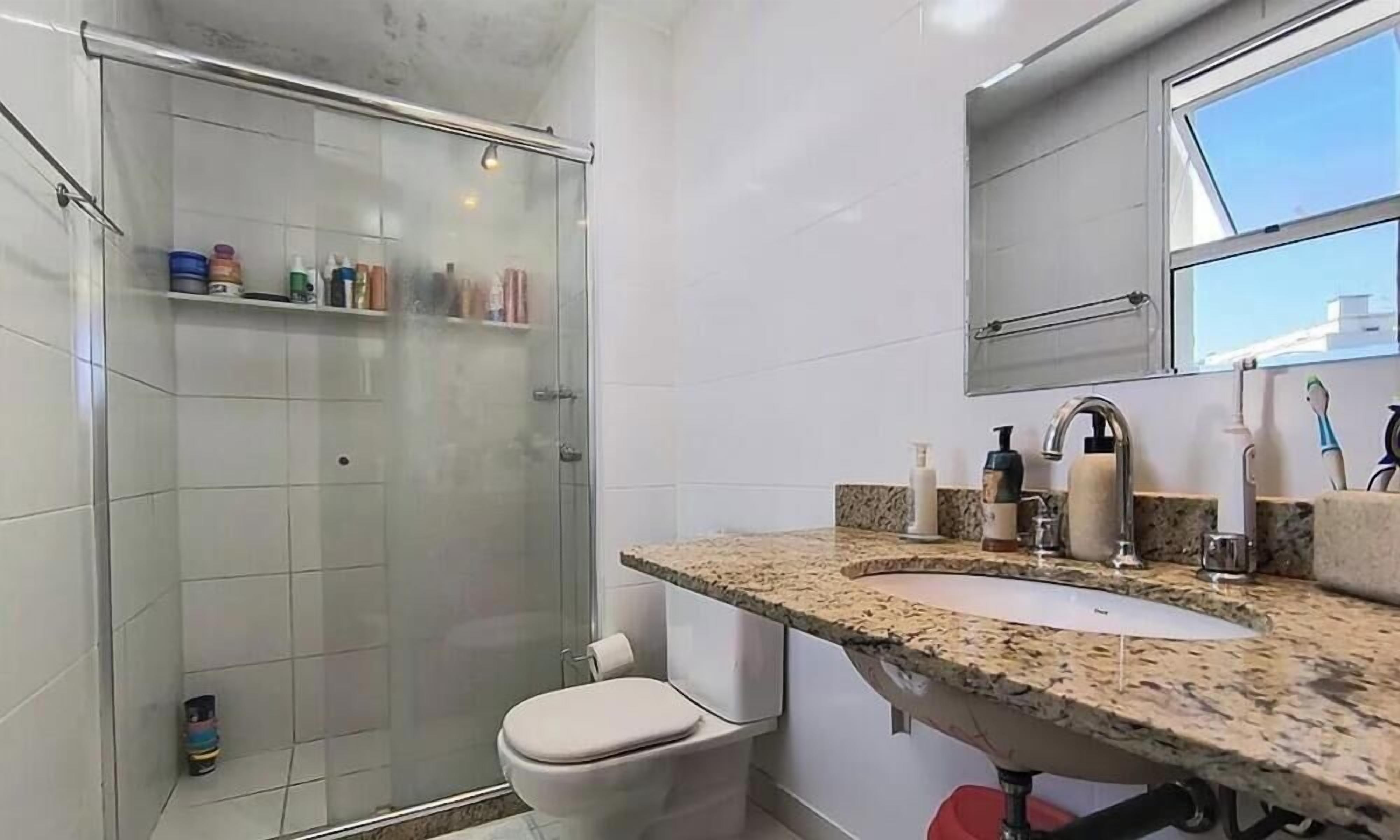 Een badkamer met een douchecabine van glas, een wit toilet, een wastafel met granieten blad en een spiegel boven de wastafel.