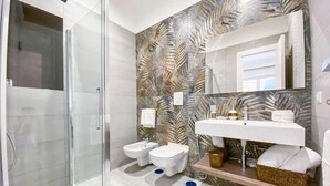 Ein modernes Badezimmer mit Duschkabine aus Glas, zwei Toiletten, einem Waschbecken mit Spiegel und einer Wandverkleidung.
