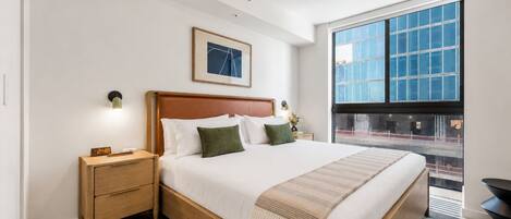 Een moderne hotelkamer met een groot bed, een nachtkastje, een wandklok, een lijst met een afbeelding en een groot raam met uitzicht.