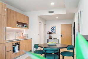 A modern kitchen with wooden cabinets, a built-in oven, and a dining area with a round table and chairs. - The Crosby Balcony 1BR by Palermo Home  (Miami)