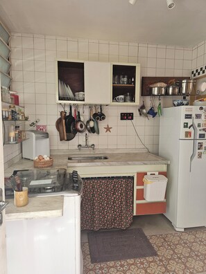 A kitchen with a tiled backsplash, a refrigerator, a sink, and various kitchen utensils and appliances. - House of Light (São Paulo)