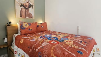 Uma cama com colcha estampada de flores, um criado-mudo com luminária e um quadro pendurado na parede.