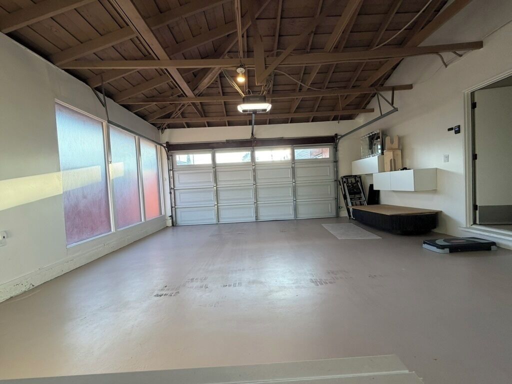 A spacious garage with a concrete floor, a wooden ceiling, and a large garage door.