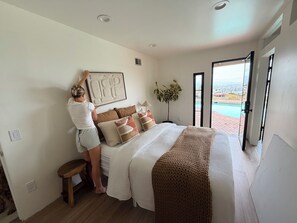 A bedroom with a bed, pillows, a bedside table, a plant, and a view of a swimming pool through an open door. -  Luxury gated villa with pool and stunning LA city views Prime Central location (Los Angeles)