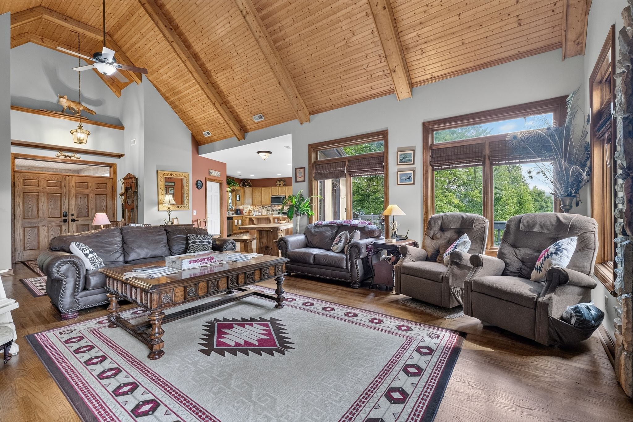 A spacious living room with a high ceiling, wooden beams, and large windows.
