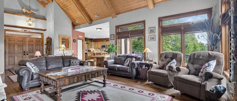 A spacious living room with a high ceiling, wooden beams, and large windows.