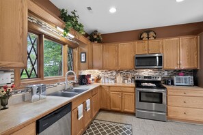 A modern kitchen with wooden cabinets, stainless steel appliances, and a window with a view of greenery. - Leatherwood MNT | Pinnacle Pt w/ 4-Stall Barn (Ferguson)