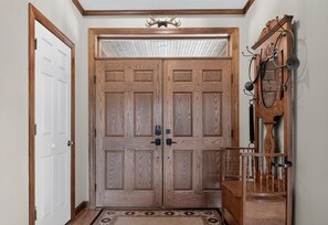 A wooden double door with a small window above it, a rug on the floor, and a wooden chair with a metal frame to the right. - Leatherwood MNT | Pinnacle Pt w/ 4-Stall Barn (Ferguson)