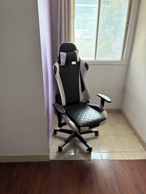 A corner office chair with a high backrest and armrests, positioned next to a window with a view of trees.