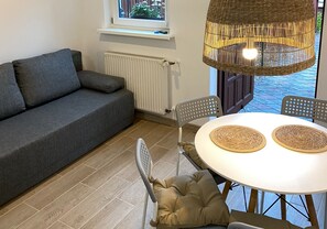 A cozy living area with a grey sofa, a round table with two woven placemats, and a wicker pendant light. - Comfortable Room for 4 People With a Kitchenette (Mielno)