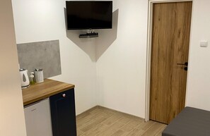 A compact room with a wooden floor, a small kitchenette with a dishwasher, a television mounted on the wall, and a wooden door. - Comfortable Room for 4 People With a Kitchenette (Mielno)