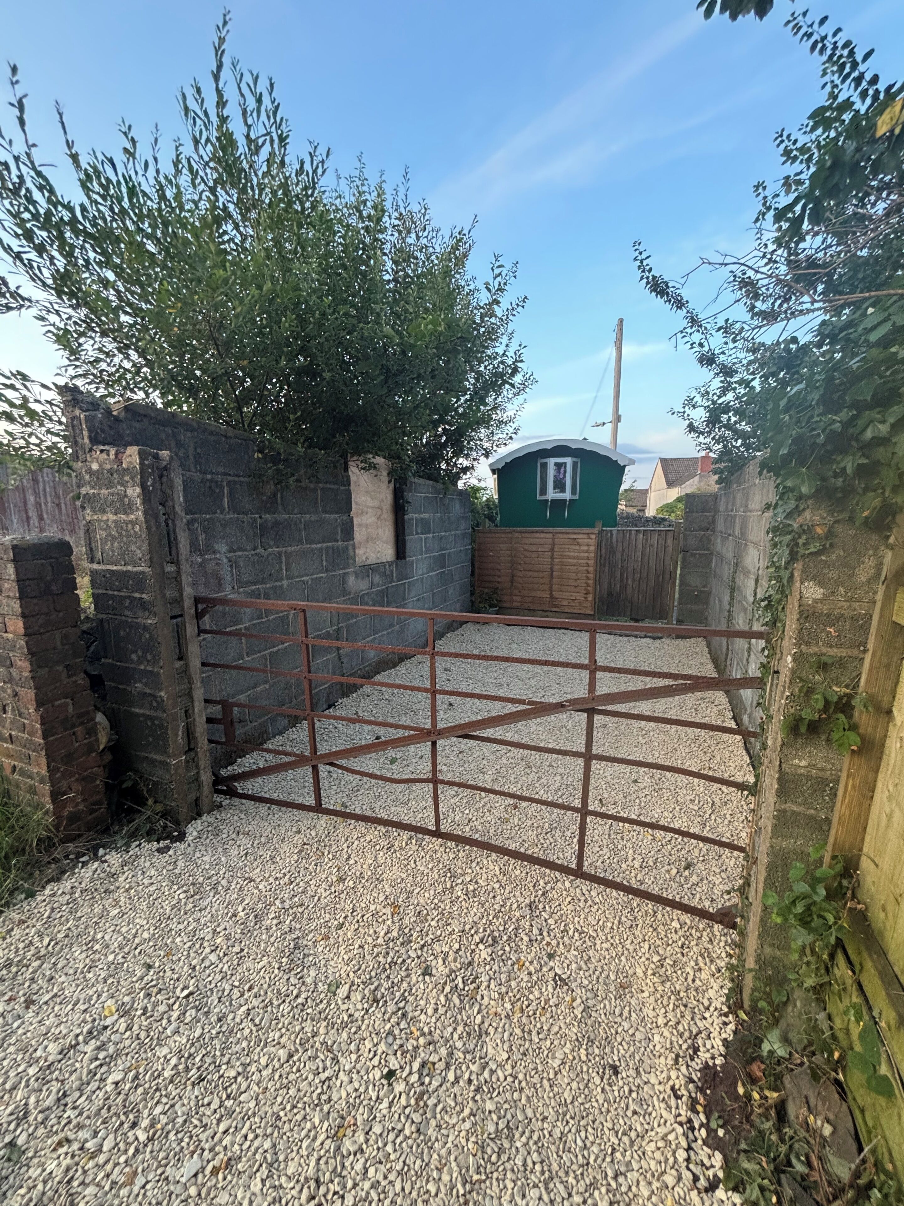 A gravel driveway leading to a gated area with a green building in the background.