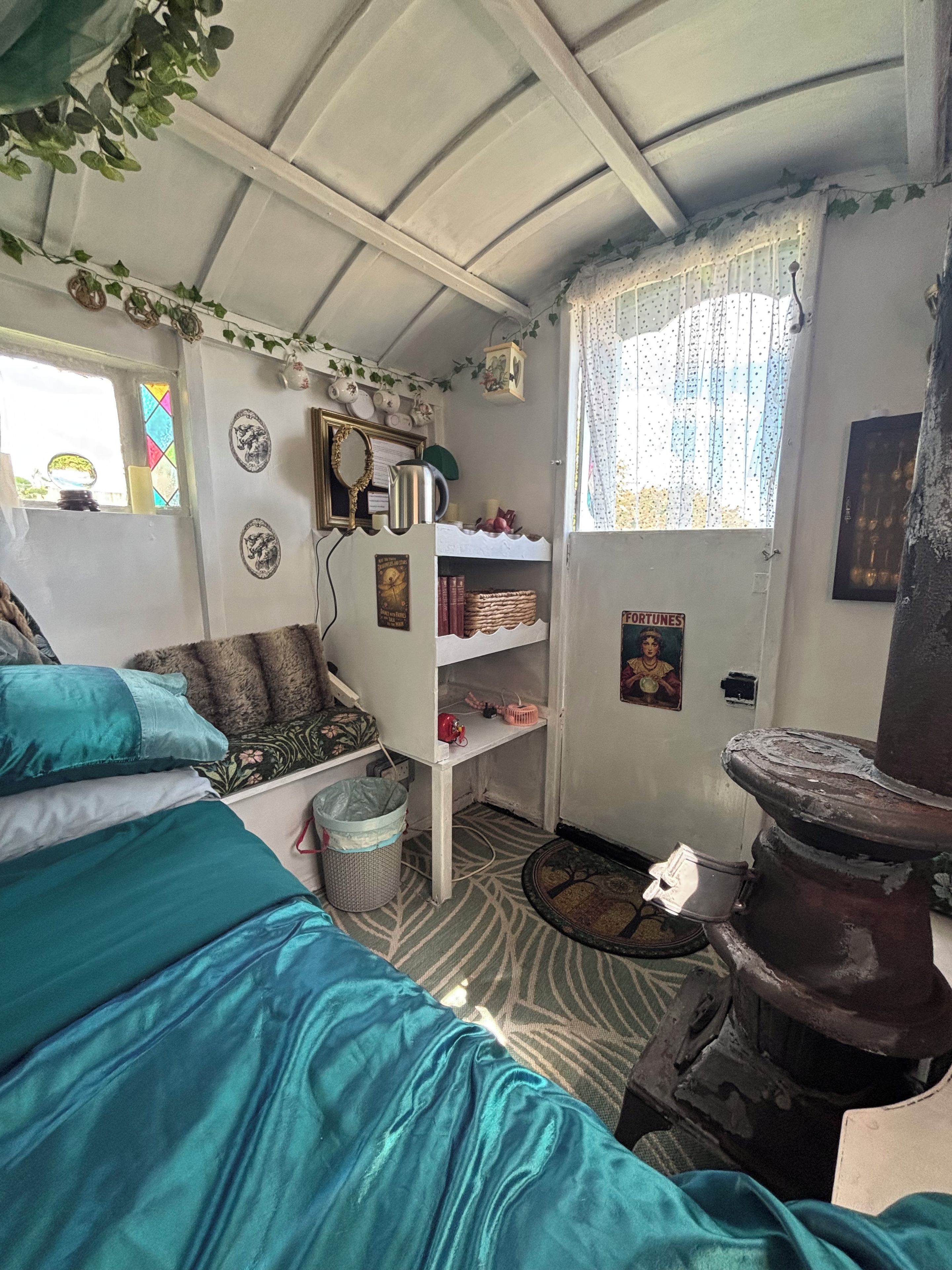Quarto com cama, prateleira com livros, janela com cortinas e parede decorada com pratos.