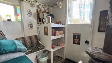Quarto com cama, prateleira com livros, janela com cortinas e parede decorada com pratos.