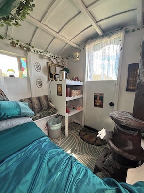 A room with a bed, a shelf with books, a window with curtains, and a wall with decorative plates.