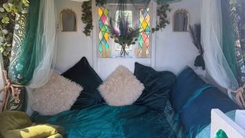 A room with a bed, pillows, a window with stained glass, and hanging plants.