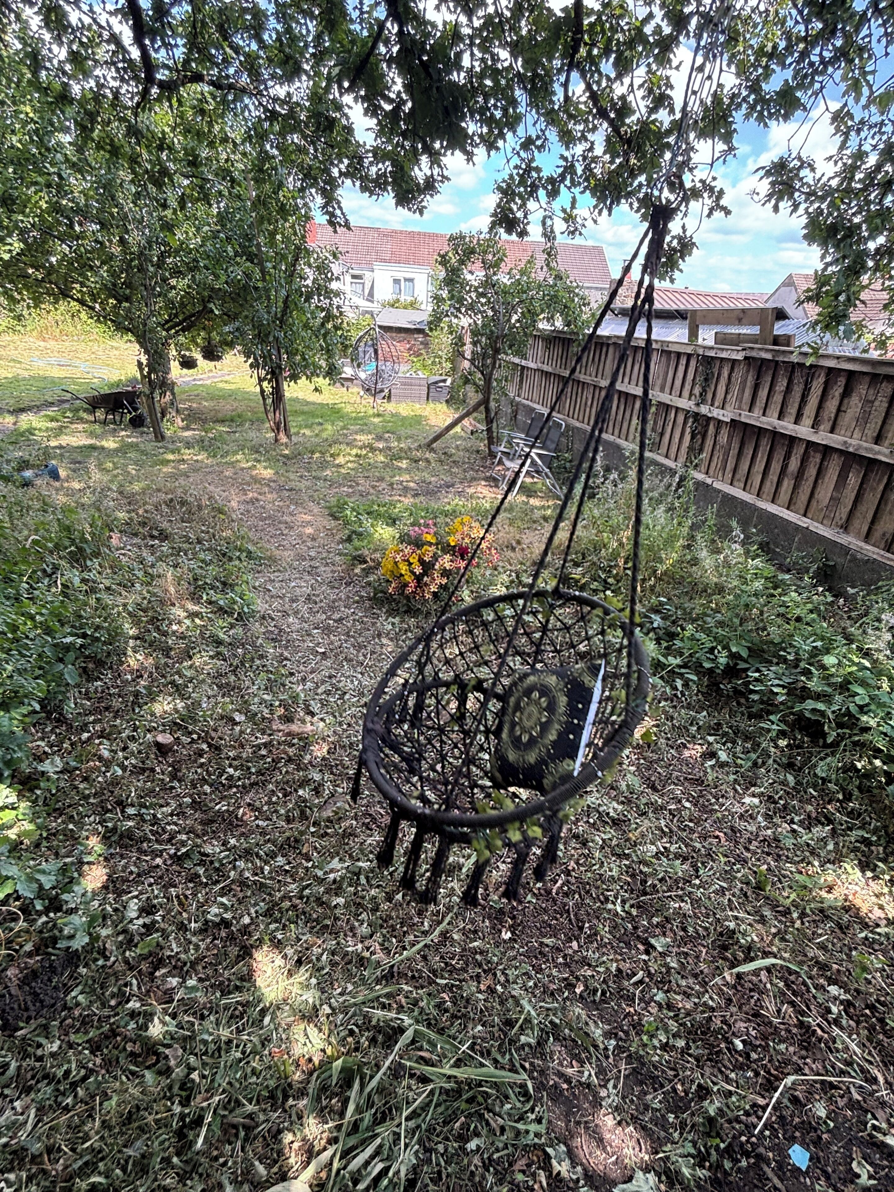 A garden with a swing set, a wooden fence, and a house in the background.