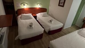 Une chambre d’hôtel avec deux lits simples, une tête de lit en bois, un mur d’accent vert et une petite table de chevet avec une lampe.